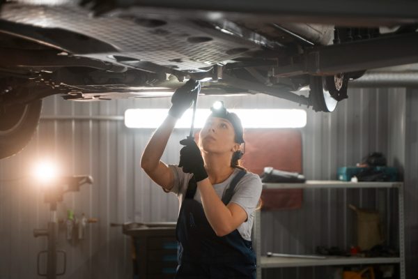 Female auto repairer working in the shop on a car Exhaust System